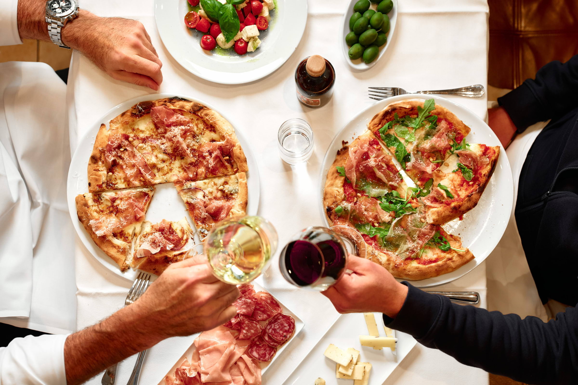 Two men toasting with wine over pizzas in a restaurant