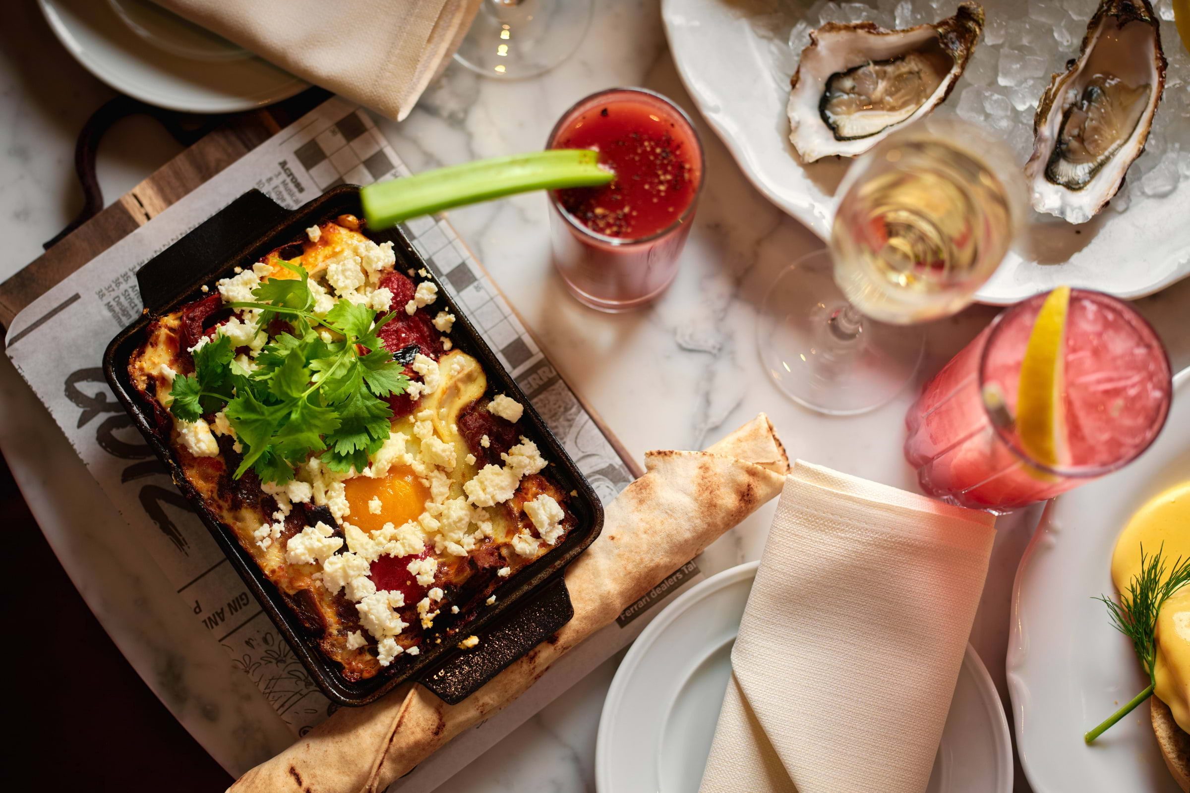 Shakshuka, a Bloody Mary, and oysters on a marble table