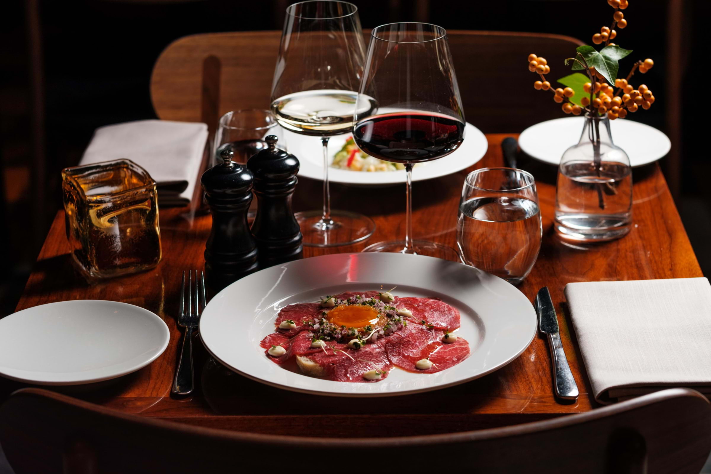A dish on a white plate, drinks, and cutlery on a wooden restaurant table